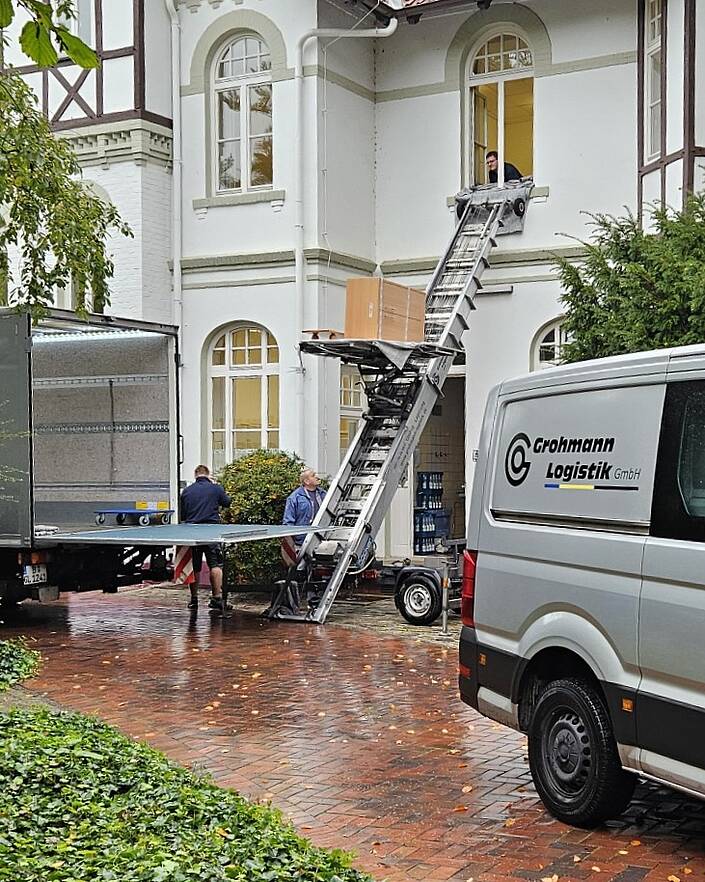 Zwei Umzugslastwagen und ein Möbellift vor Hausfassade